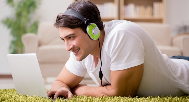 Young man lying on floor listening to music on laptop