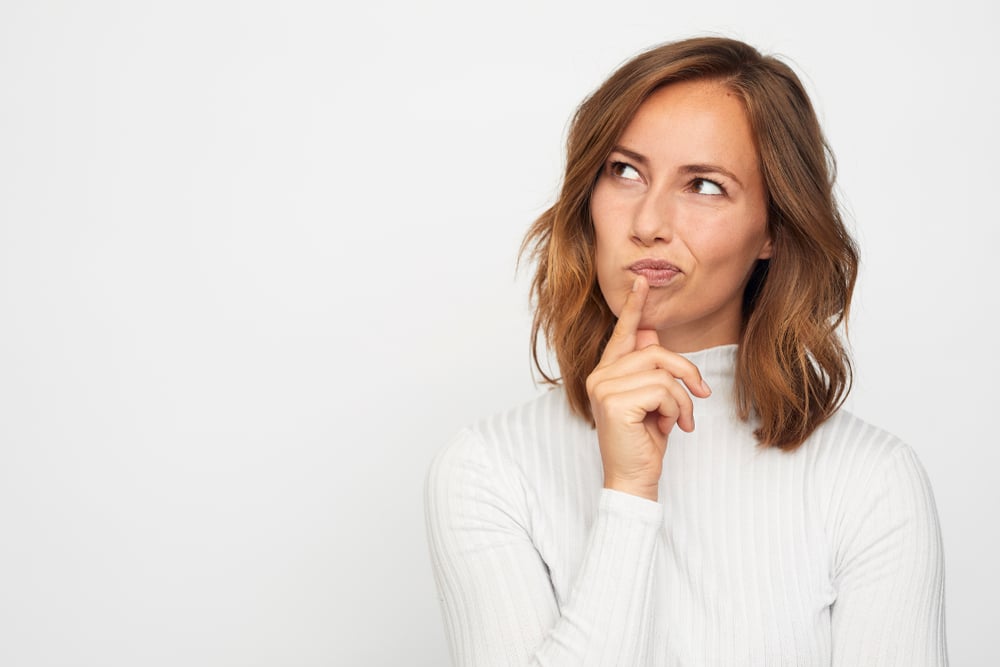 woman in white jumper thinking about investing in the ftse 100